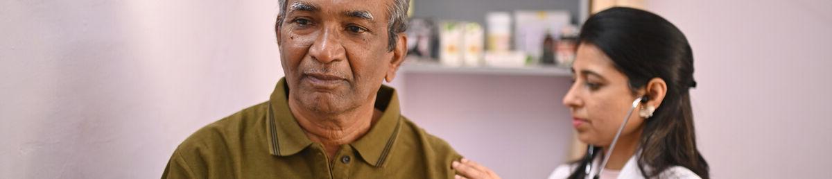 Health practitioner holding a stethoscope against an older patient’s back